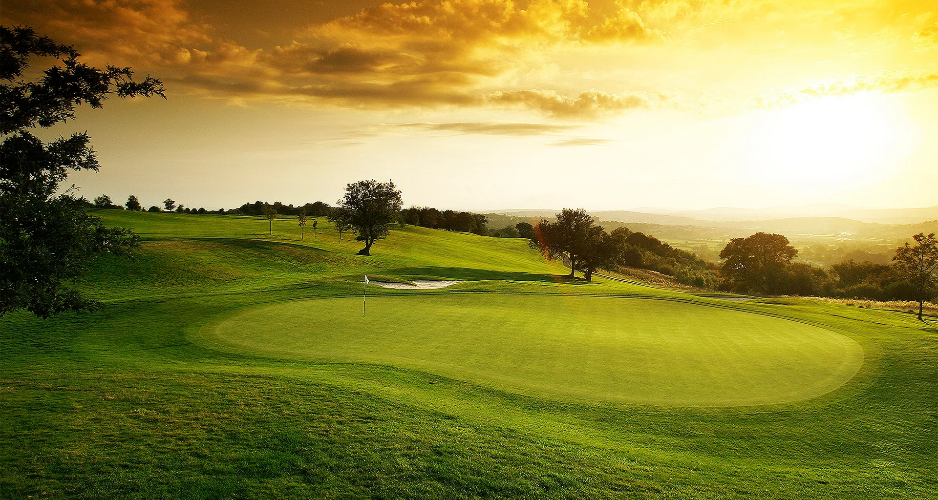 A general view of a green and bunker at Celtic Manor with the sky turned orange as the sun rises.