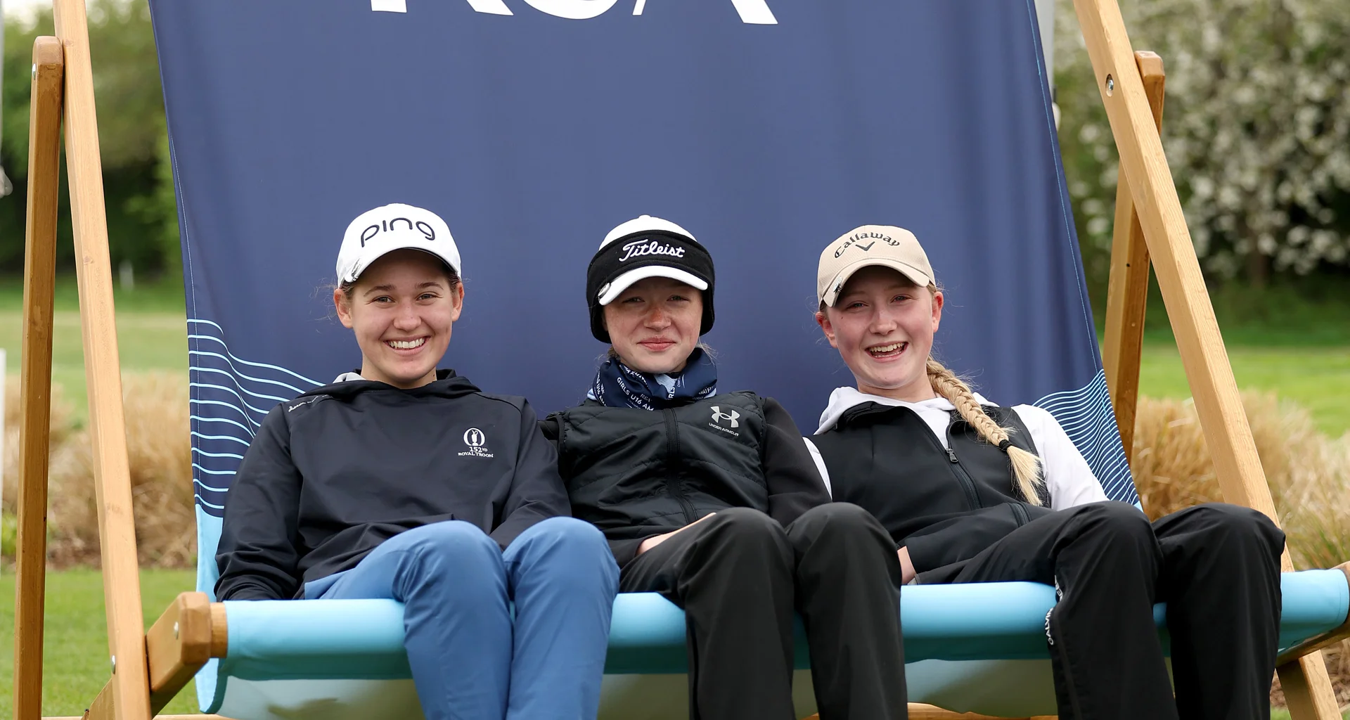 Three teenage girls sit on a giant deckchair at the AIG Women's Open.