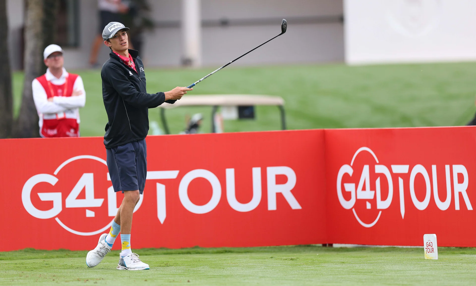 Guy Harrison stands infront of a red sign which says 'G4D Tour' after playing a tee shot.