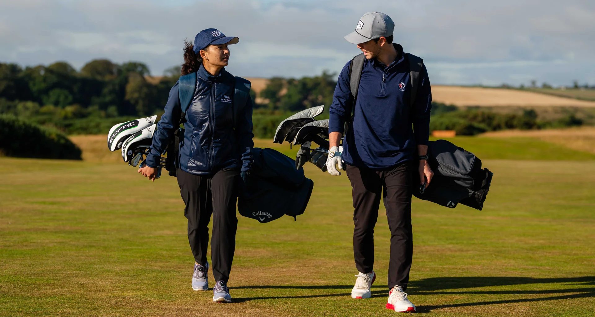 Two golfers walk on a course carrying golf club bags during an R&A Scholarship Leadership Conference event in St Andrews.