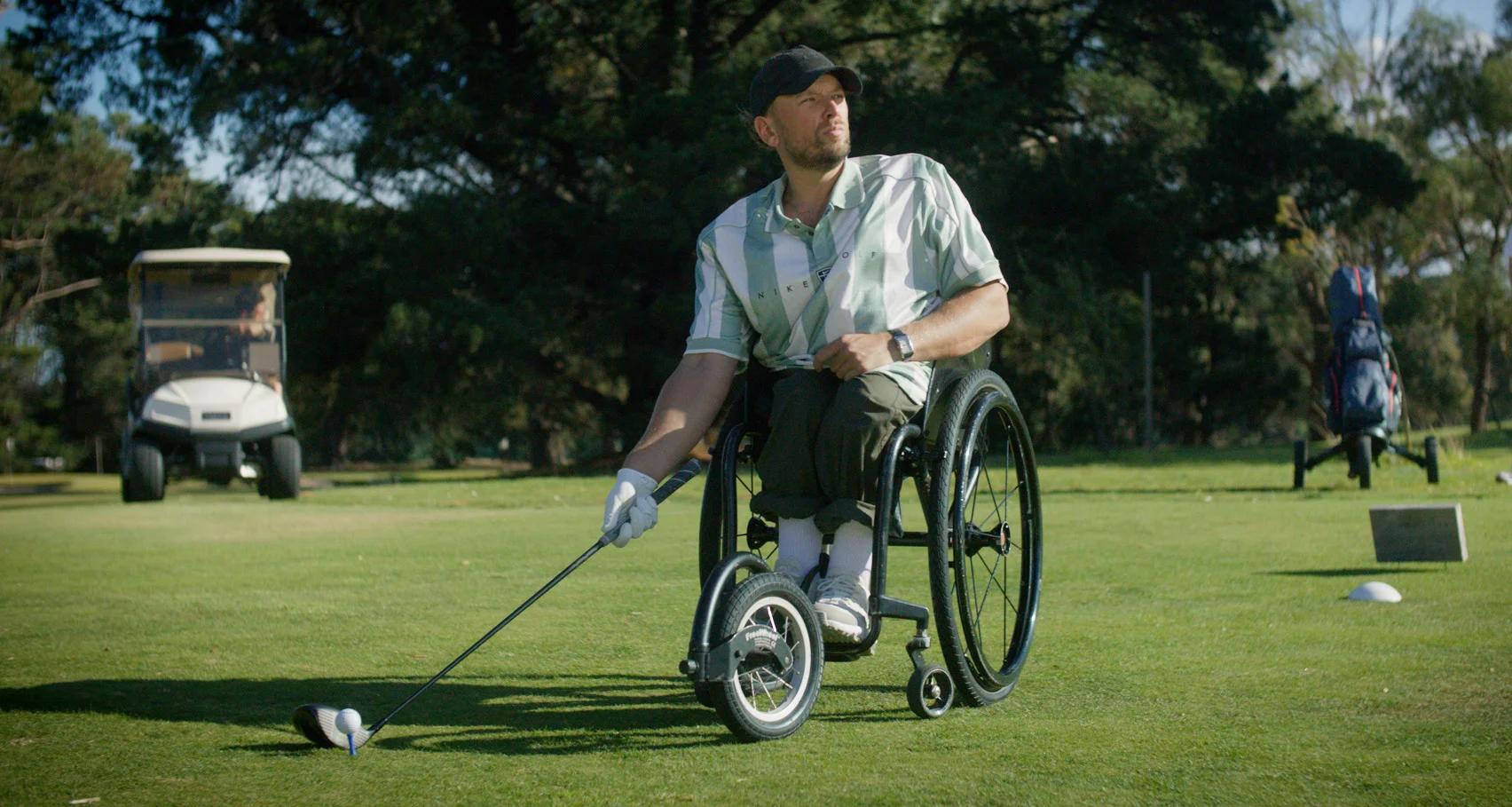 A man in a wheelchair teeing up to hit a drive on a golf course.
