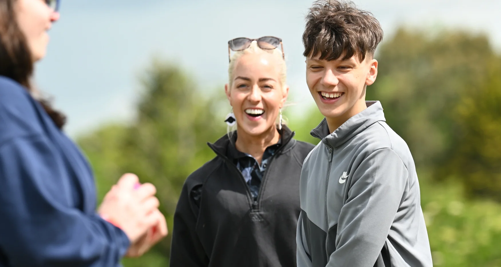 A child faces the camera smiling with a golf instructor standing behind him.