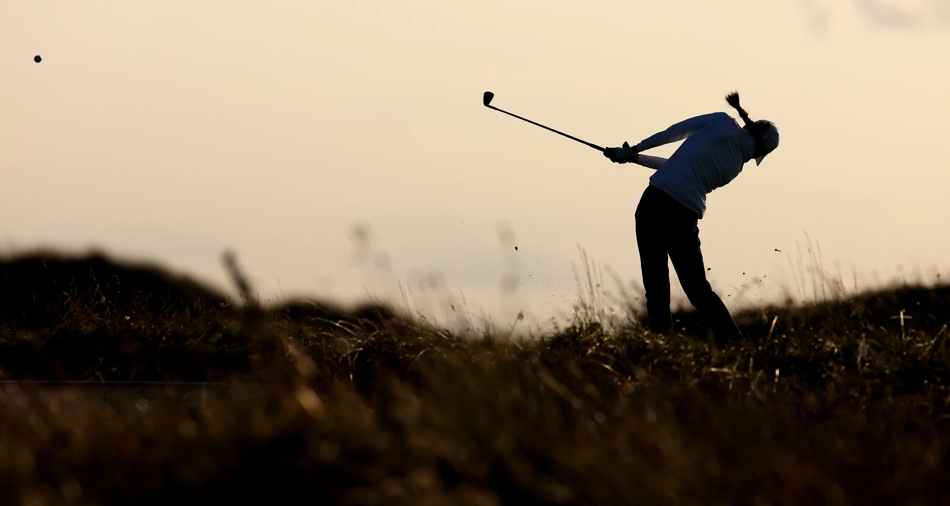 A silhouette of a female golfer playing a shot from the rough.