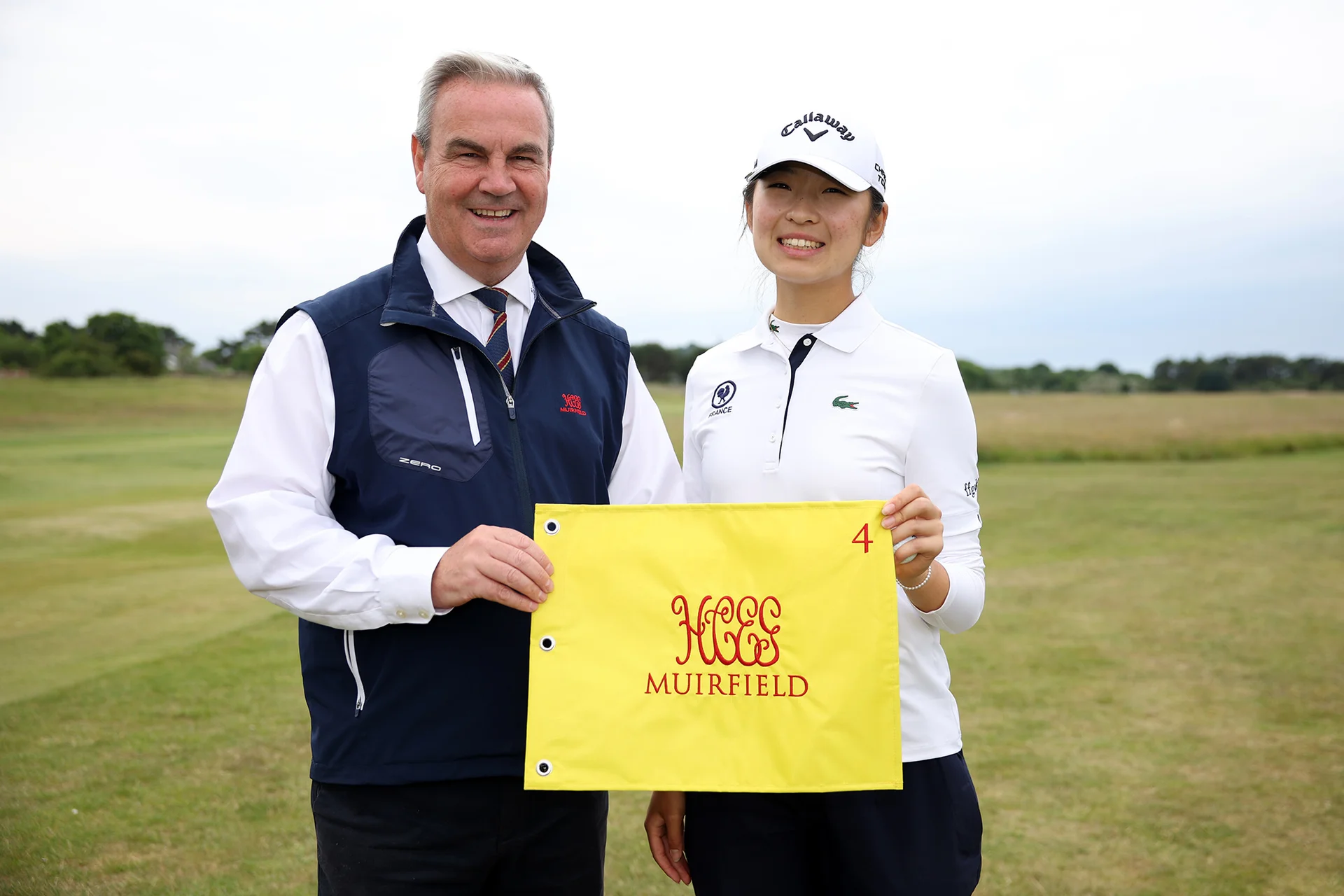 Giselle Zhao of France is presented with a Muirfield flag by Secretary of the Honourable Company of Edinburgh Golfers Stuart McEwan after her hole in one on the 4th hole during Day one of the 2026 Women's Amateur Championship at Muirfield.