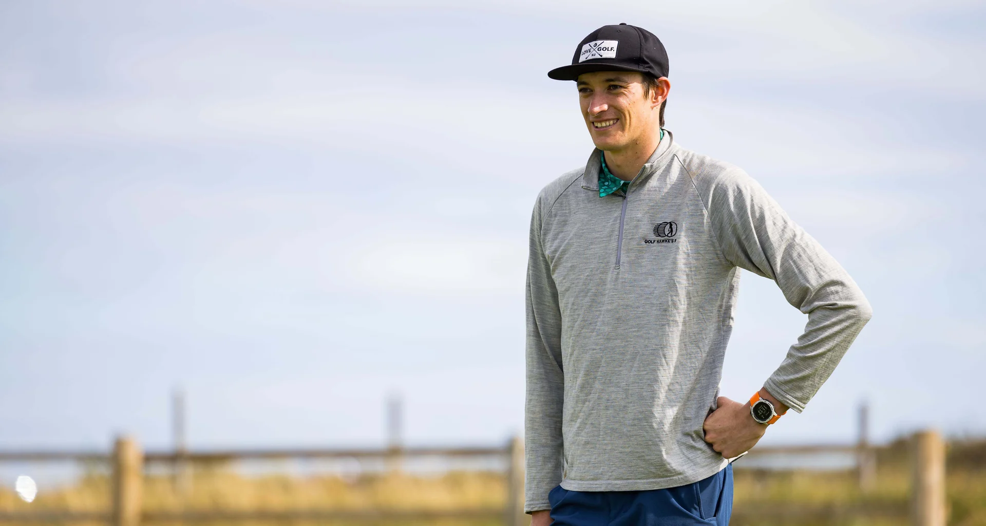 Guy Harrison stands wearing a pair of shorts and sweatshirt, holding a golf club in his right hand.
