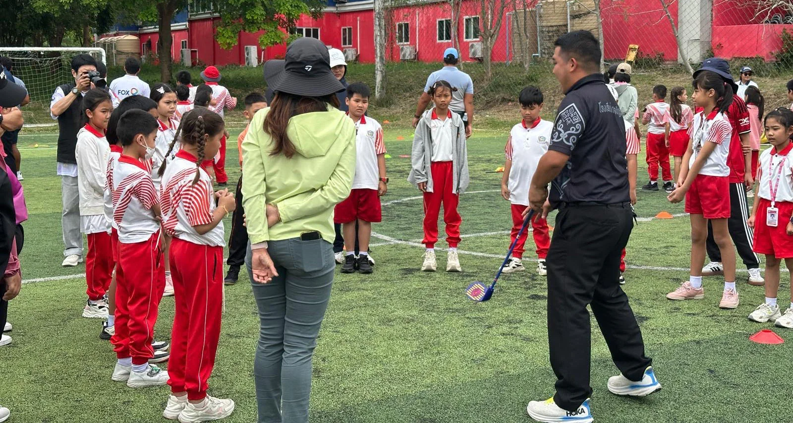 Children stand in a group listening to an instructor as part of the Community Golf Instructor Programme.