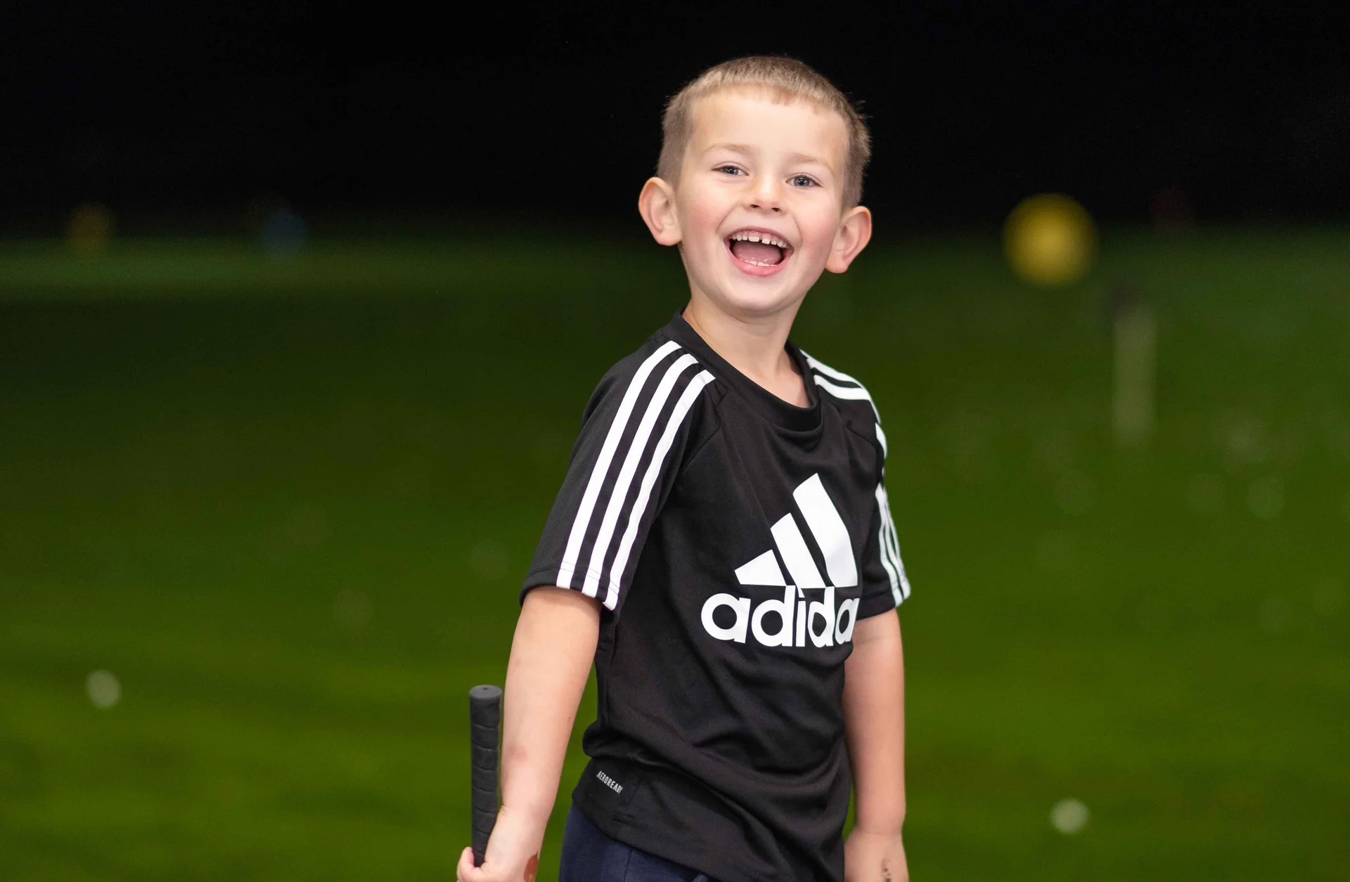 A young boy smiling as he plays golf at a driving range.