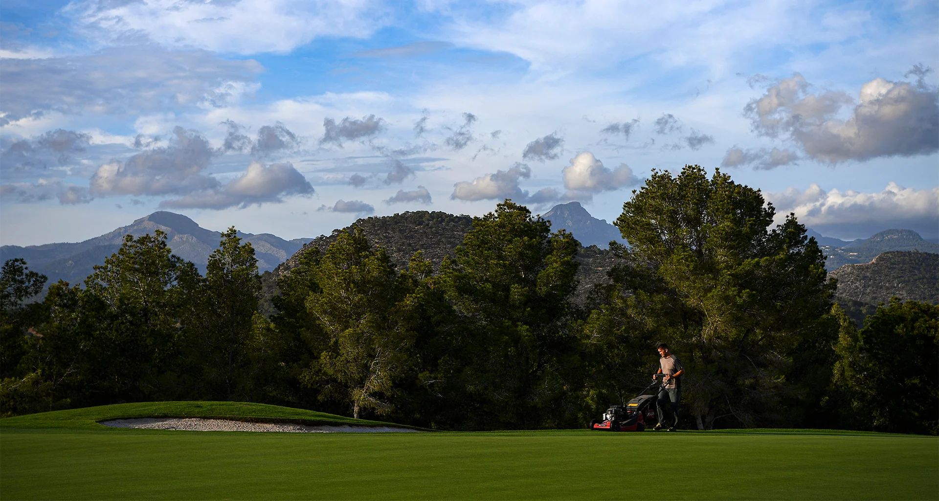 A greenkeeper with a lawnmower on a golf green.