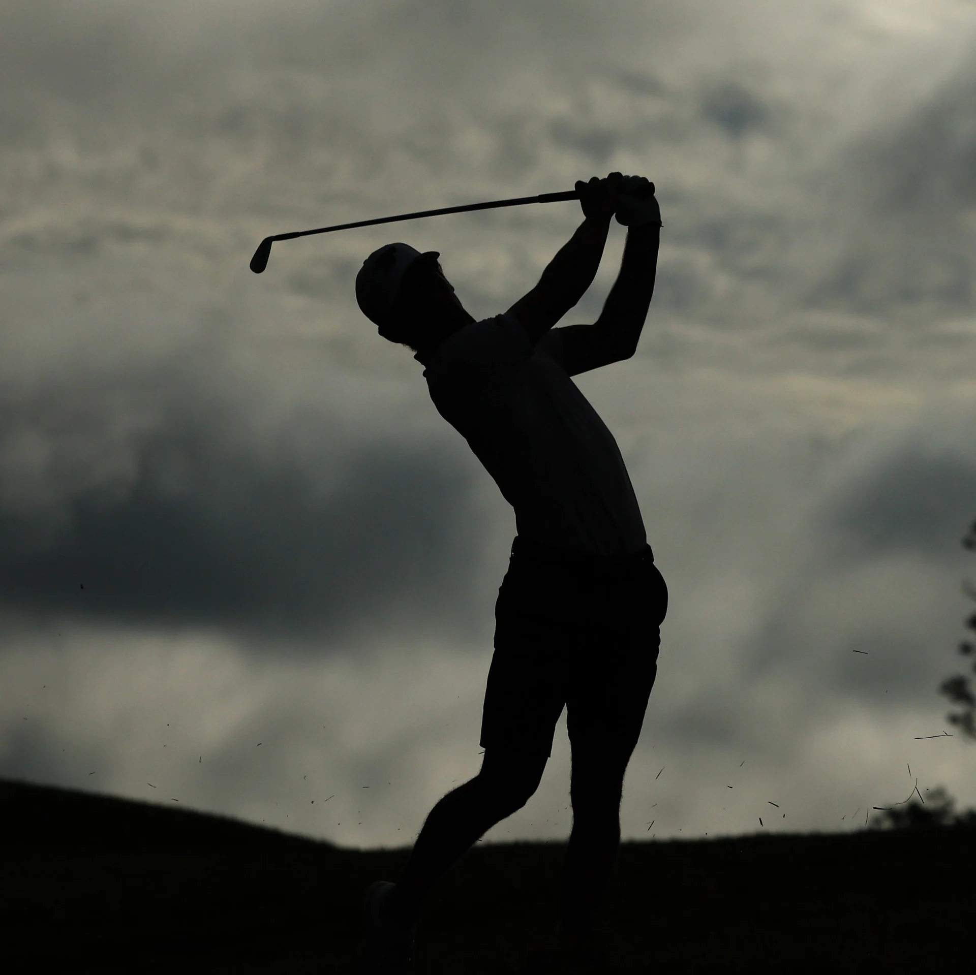 A silhouette of a male golfer who has just completed her swing, set against a cloudy sky.