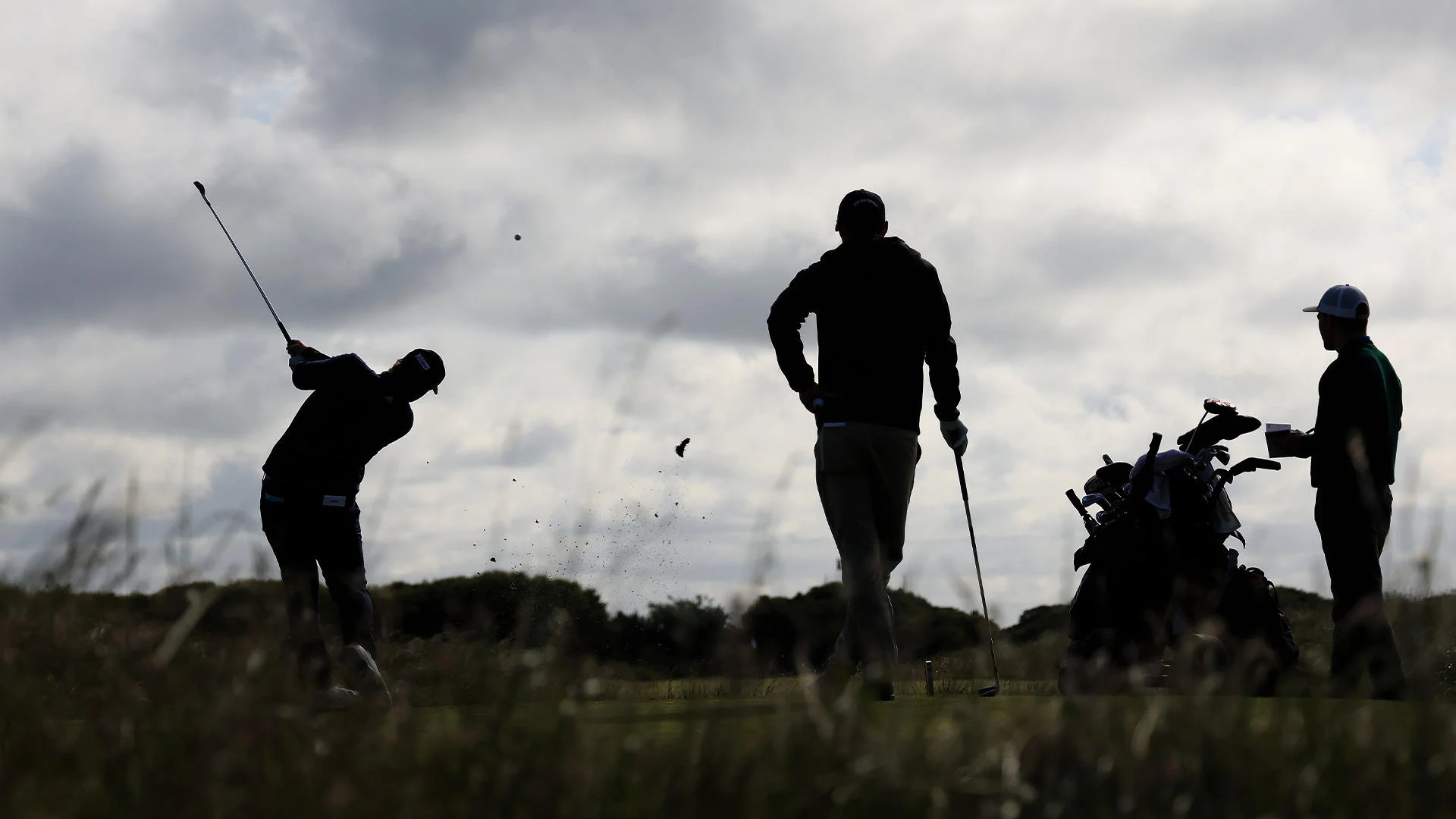 The silhouettes of three people: one has just hit a golf shot while two others watch on. 
