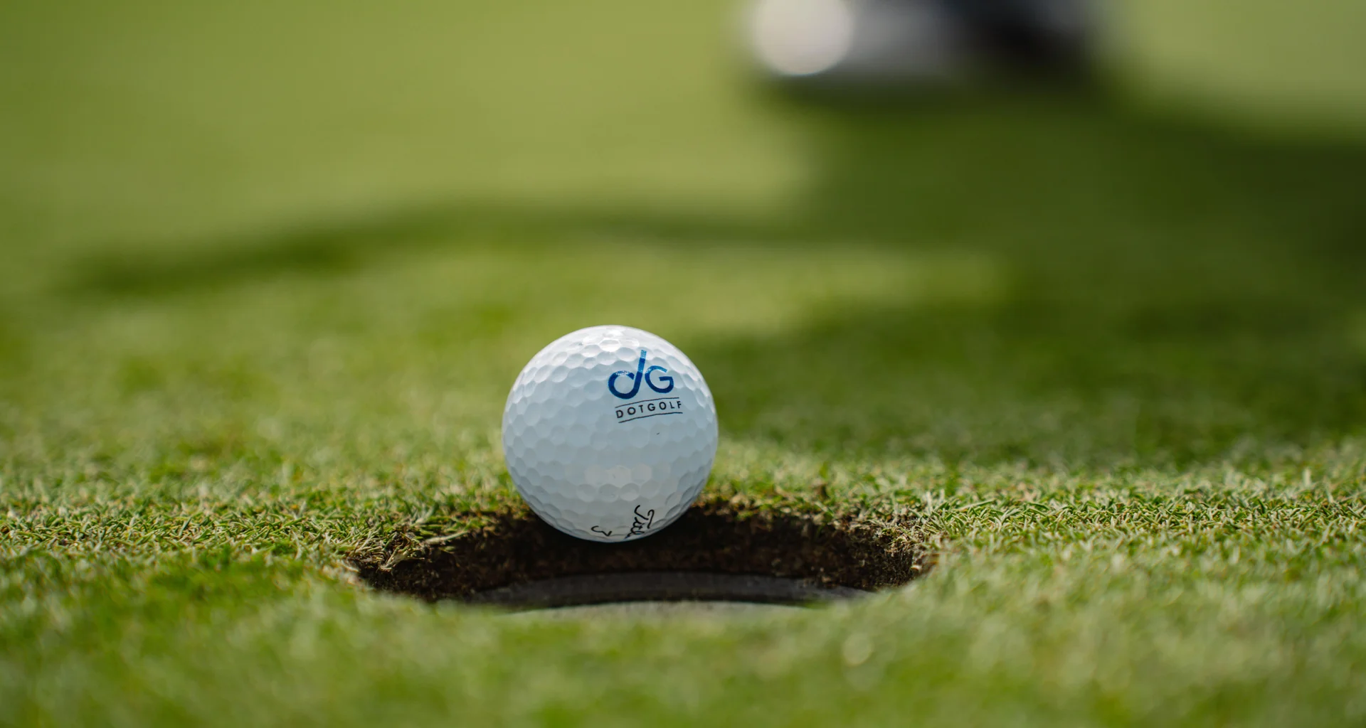 A golf ball - emblazoned with DotGolf branding - is about to fall into a golf hole.