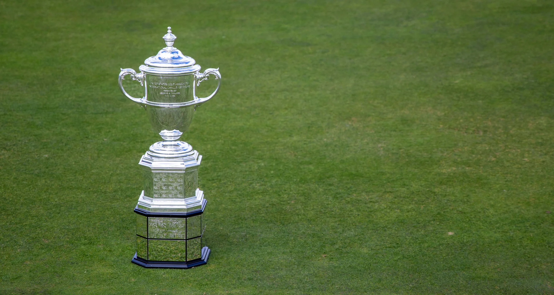 A detailed view of the Walker Cup trophy on green grass.