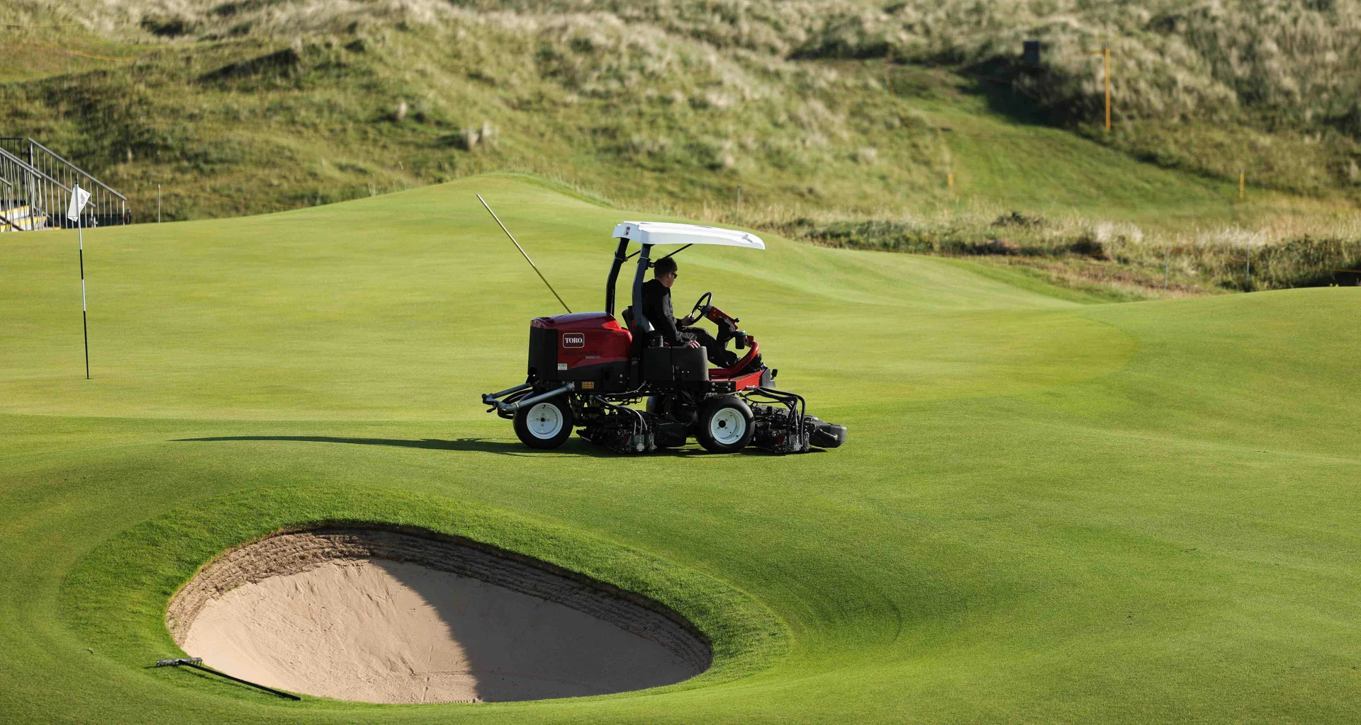A greenkeeper on a motorised lawnmower carries out work on a golf green.