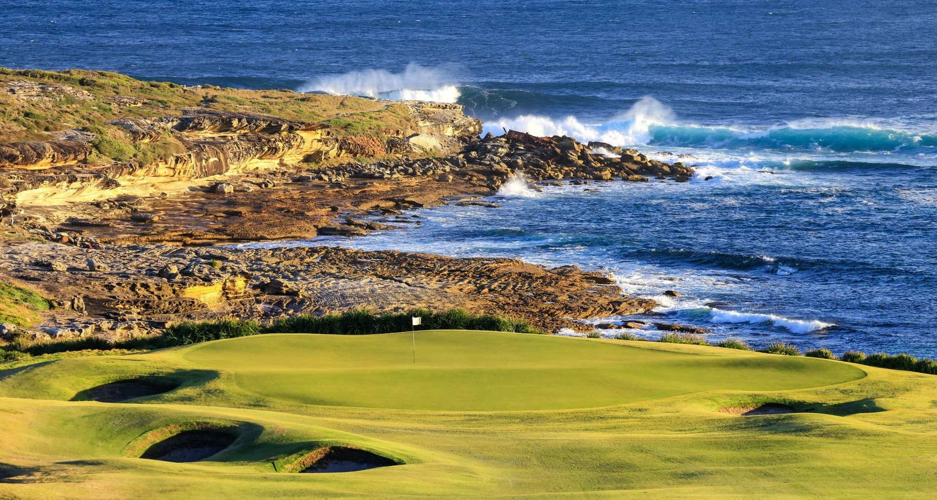 An image looking towards a golf green at New South Wales with a rugged coastline in the background.