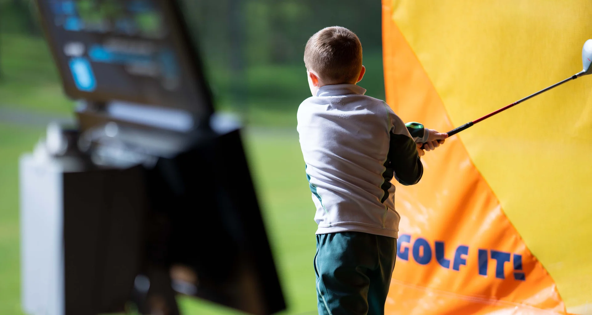 A boy swings a golf club in a driving range bay at Golf It!