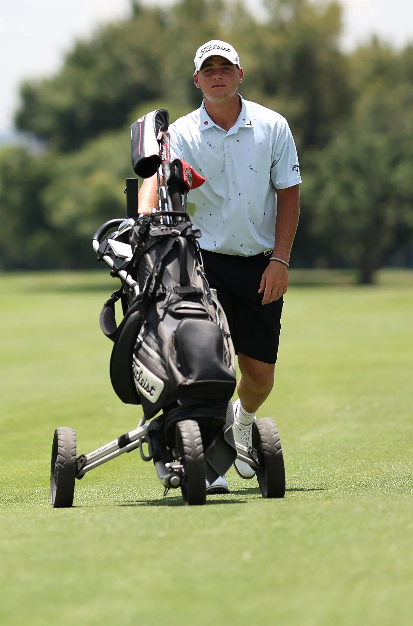 A golfer pushes his golf bag and trolley down a fairway.
