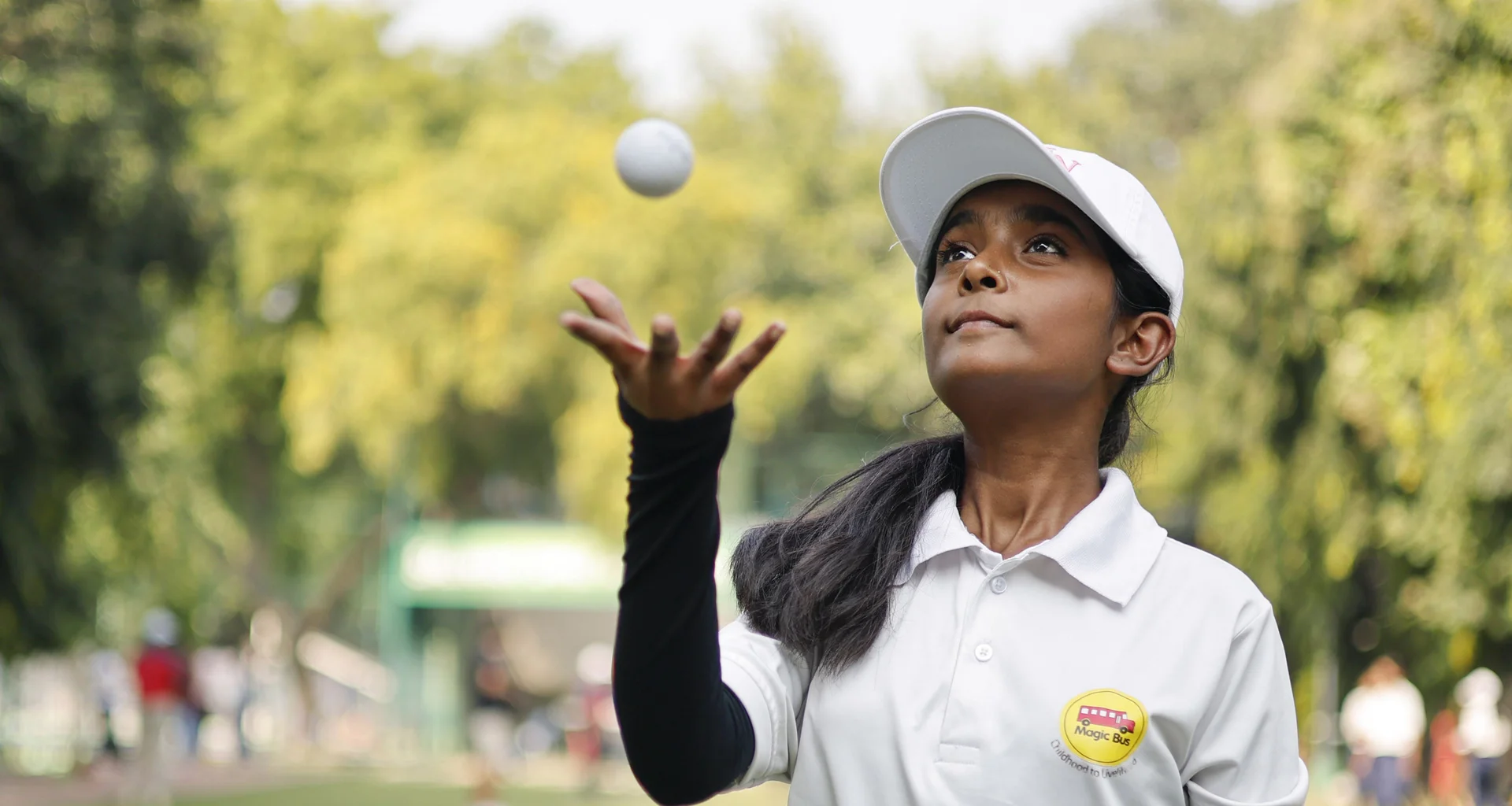 A young girl wearing a 'Magic Bus' t-shirt tosses a golf ball in the air.