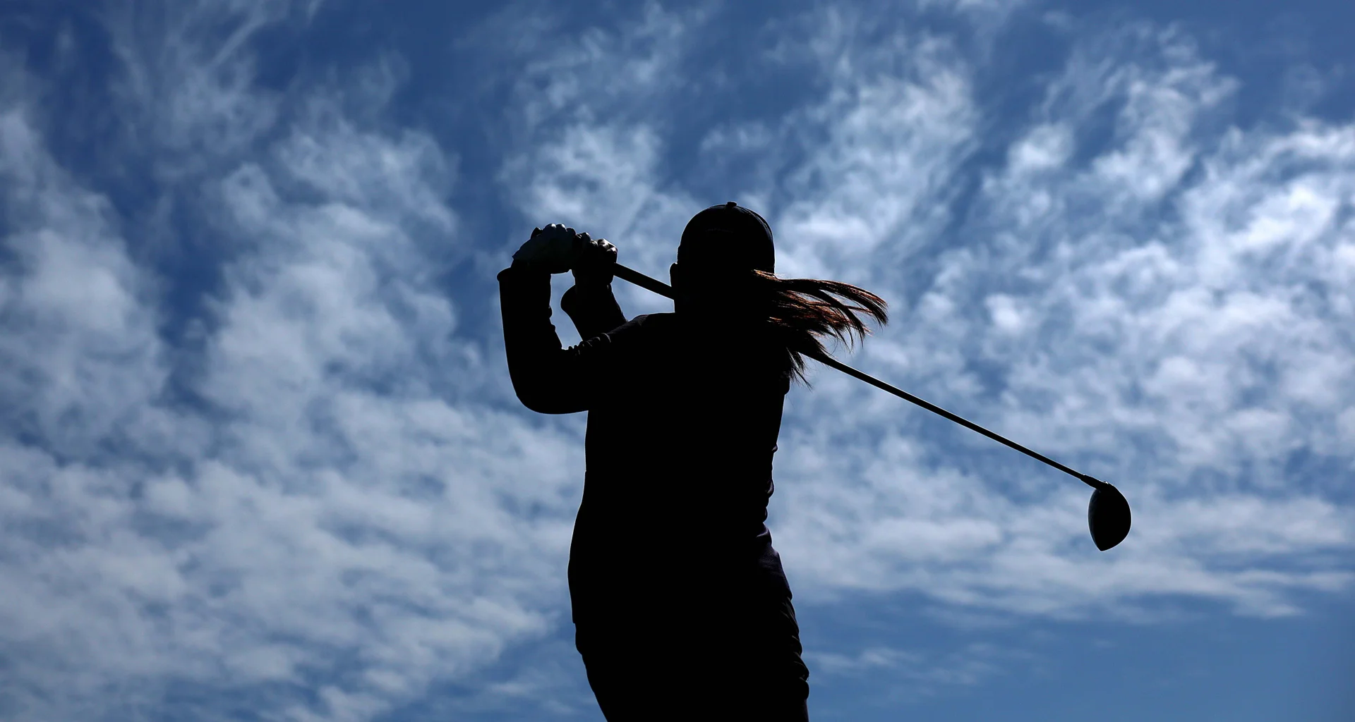 A silhouette of a female golfer who has just completed her swing, set against a blue sky.