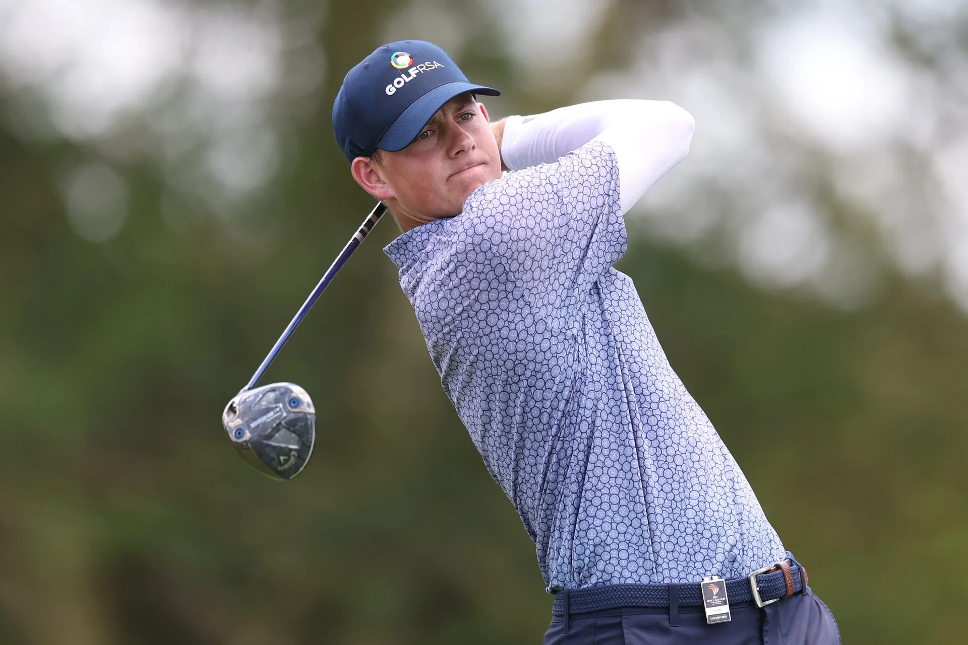 A man looks on in focus after taking a golf shot.