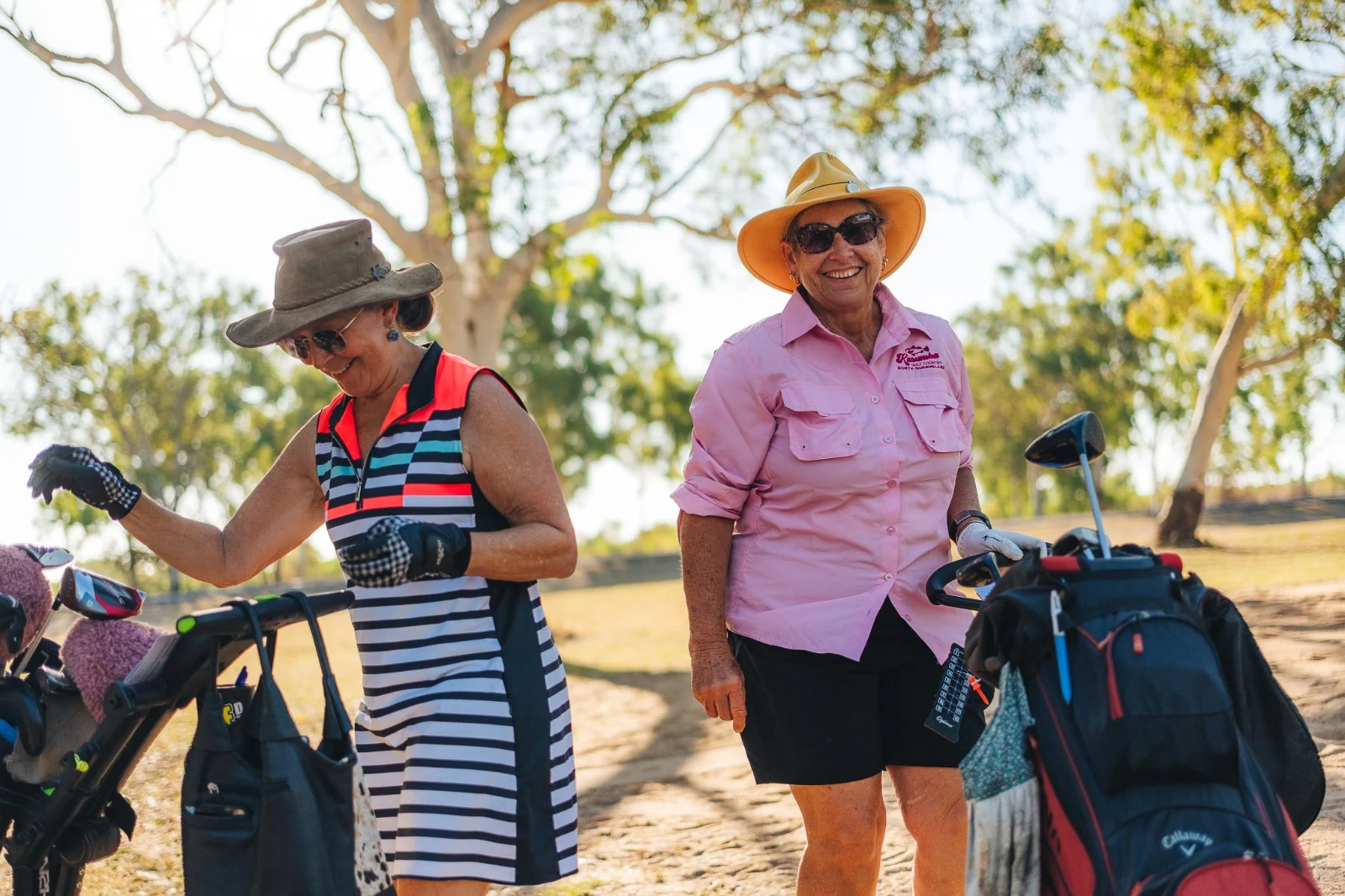 Two older women smiling and wearing sun hats and sun glasses while playing golf.