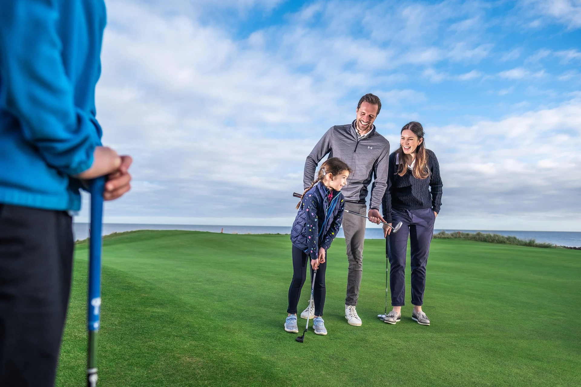 A man, woman and young girl stand together smiling on the green of a golf course.