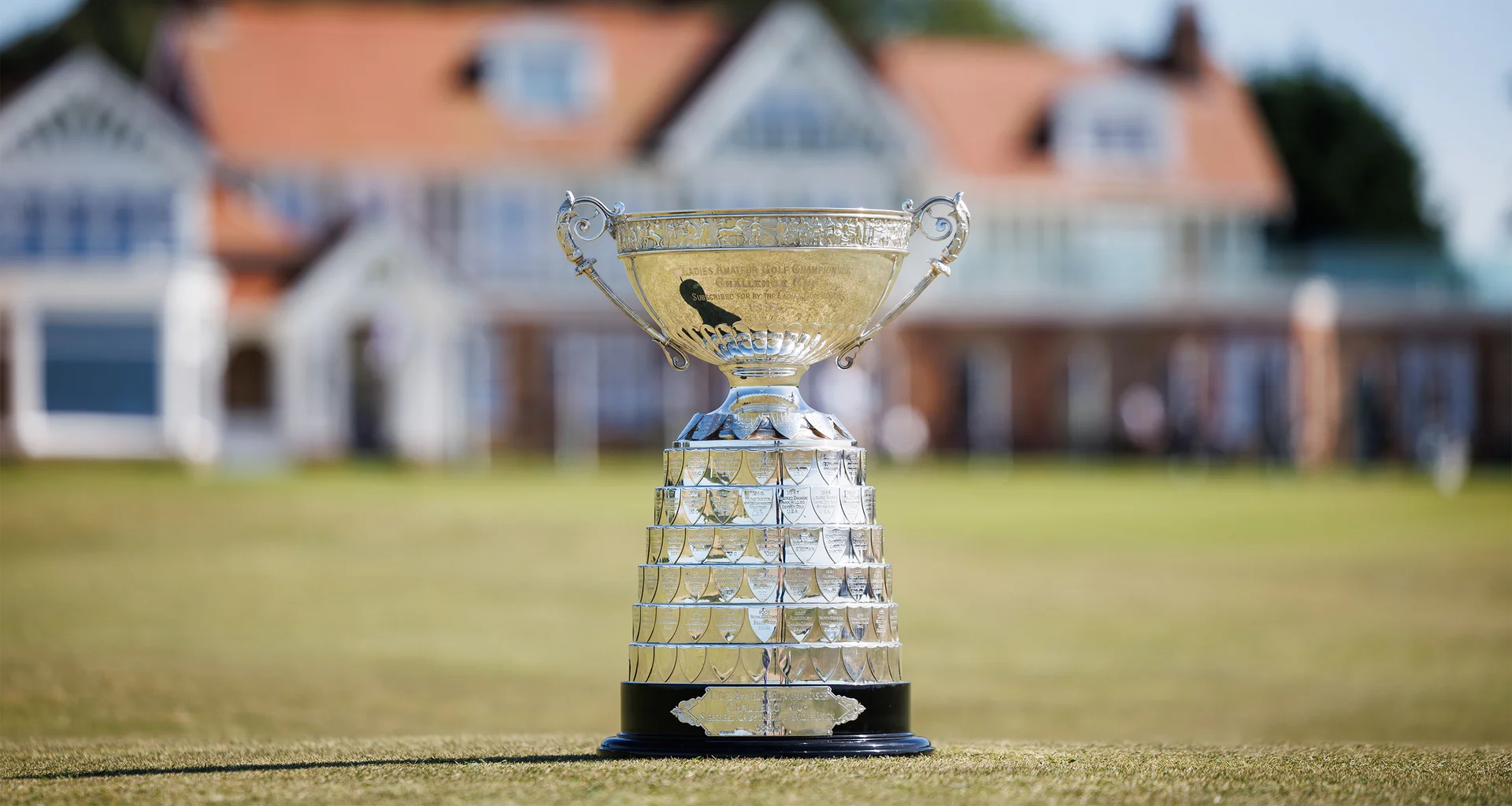 The Women's Amateur Championship trophy sits on grass in front of the Muirfield Golf Club clubhouse.