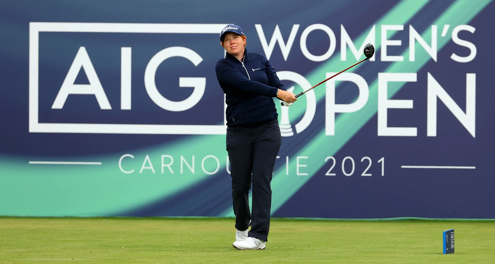 Felicity Johnson tees off in front of a large sign which reads AIG Women's Open Carnoustie 2021.